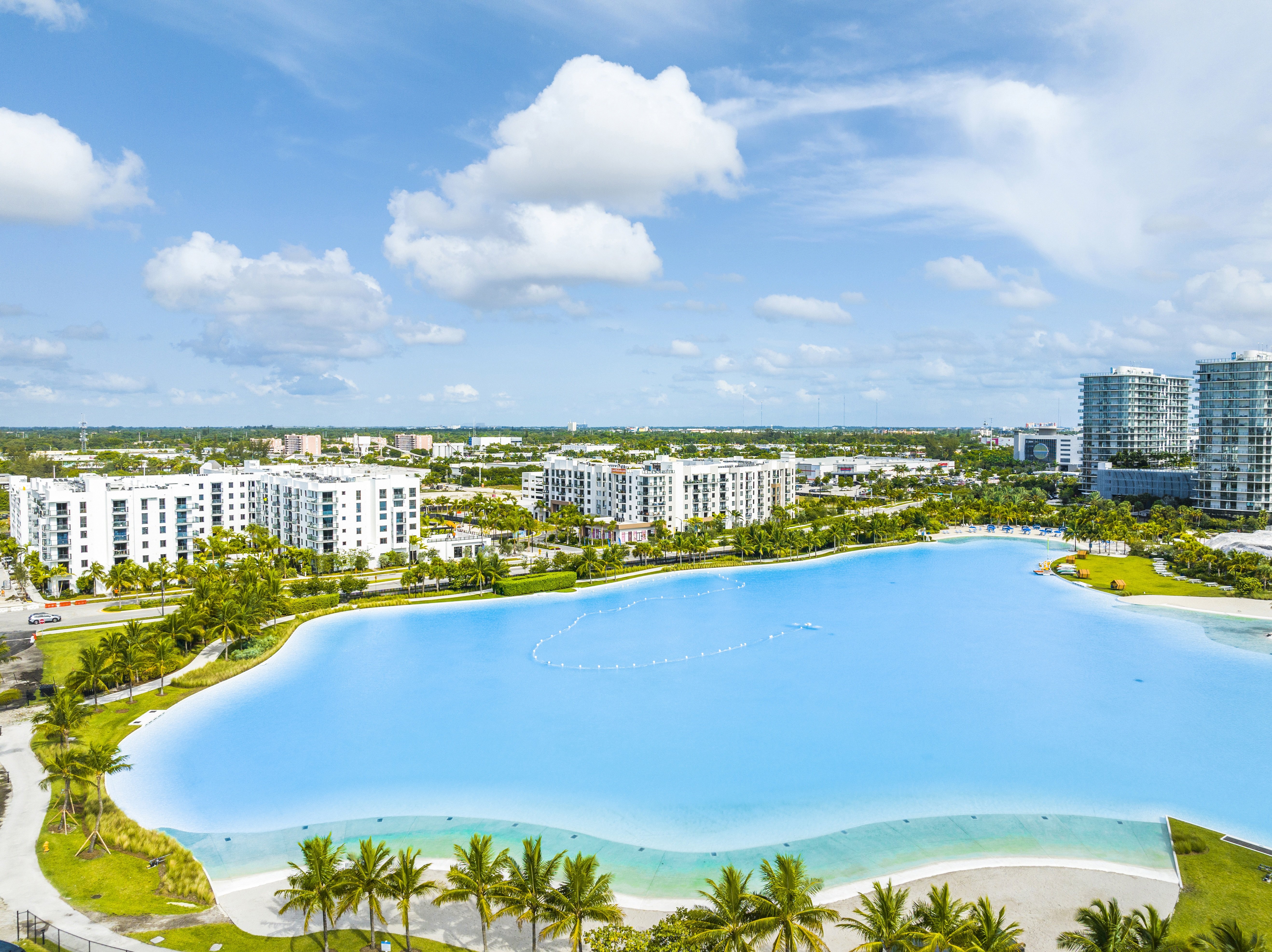 A large swimming pool surrounded by palm trees and buildings.